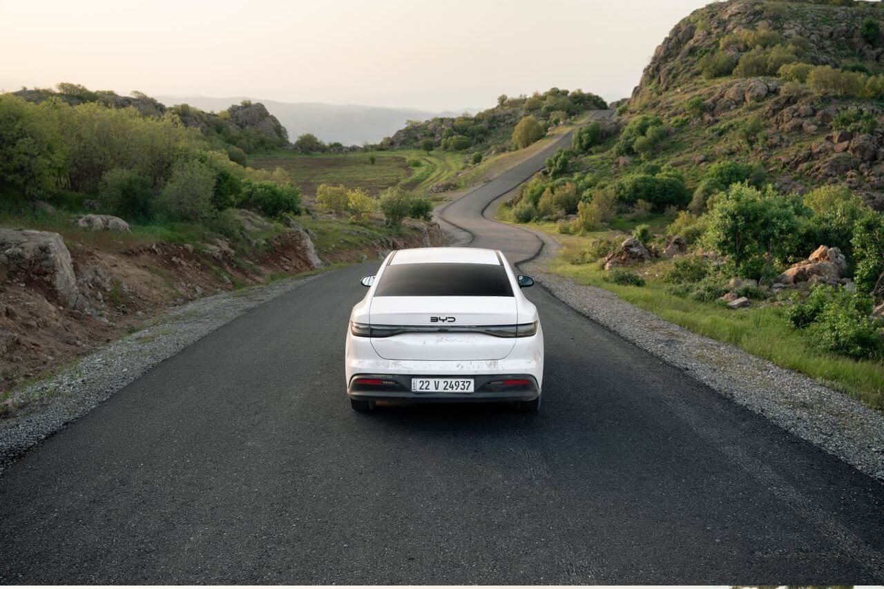 An electric car driving towards a winding road through hilly countryside