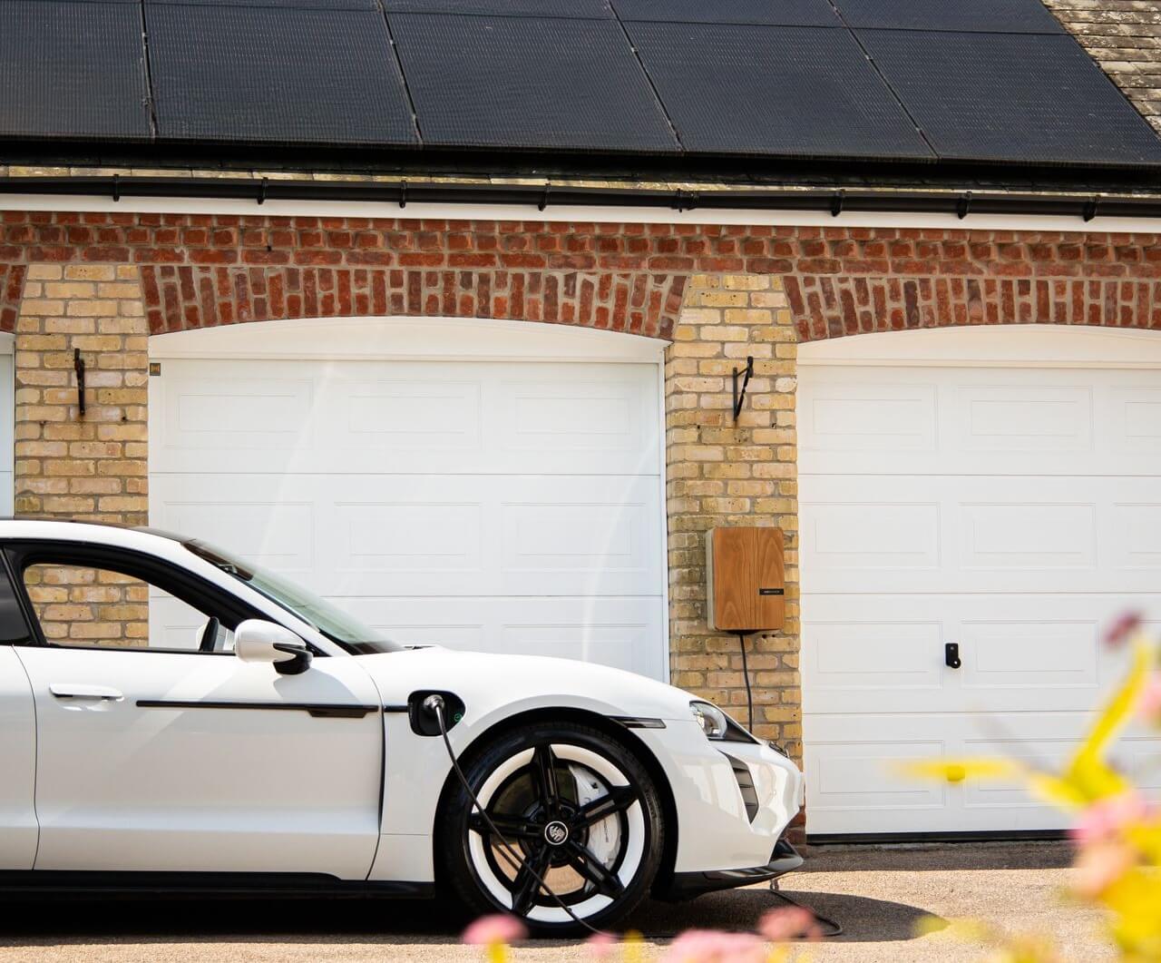 An electric car charging beside a home with rooftop solar panels