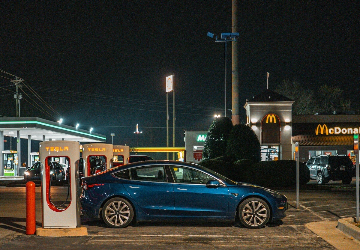 An electric car connected to a public fast charger beside a restaurant at night