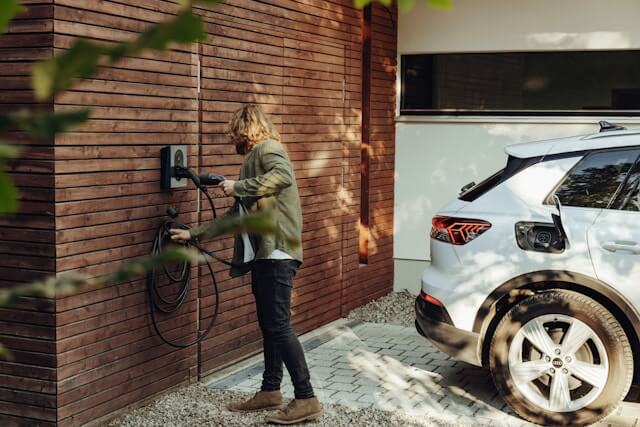 A driver taking the charging lead from a fixed Mode 3 wallbox beside an EV